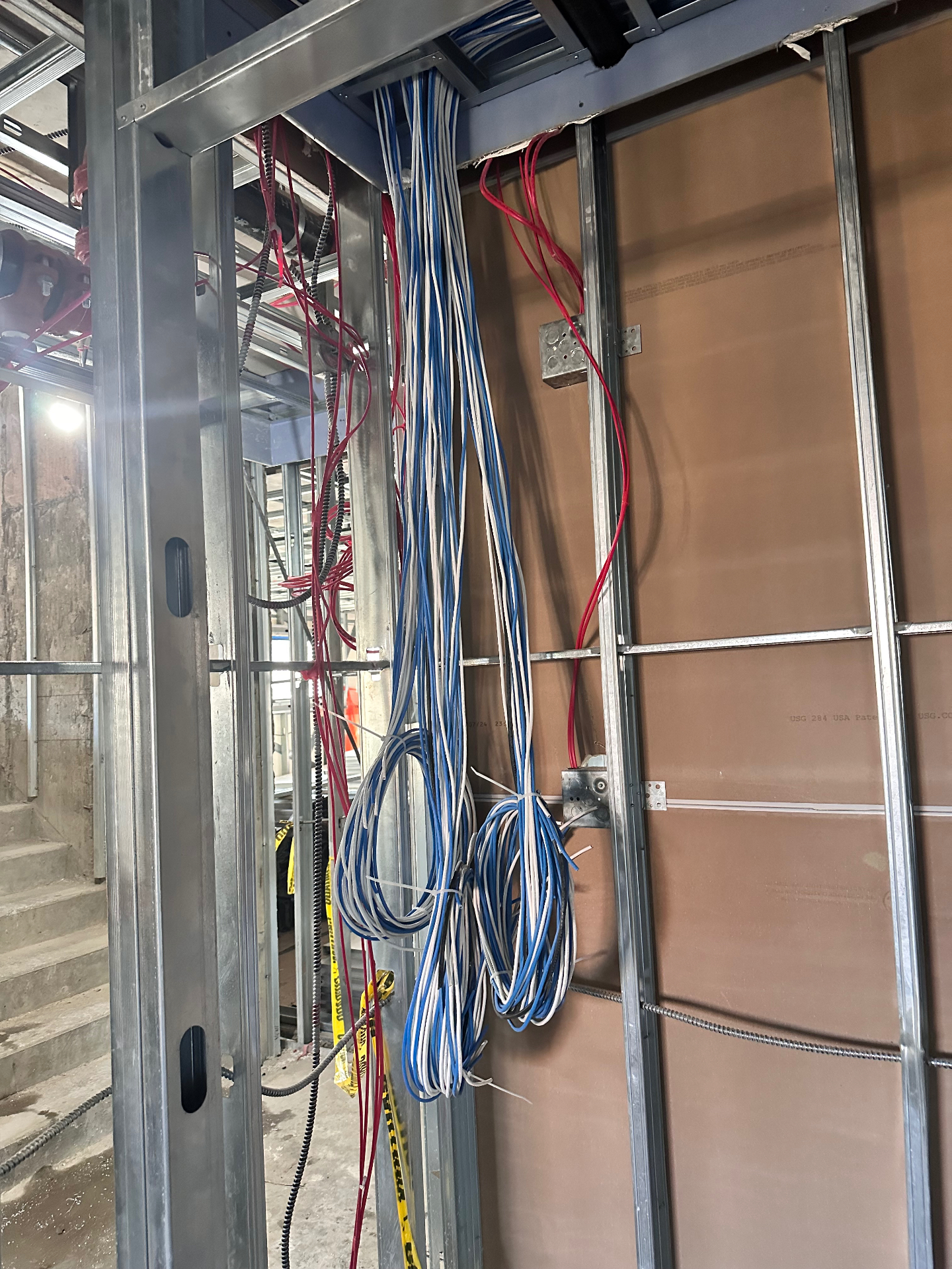 Low voltage riser cabling routed through metal stud framing beside electrical boxes